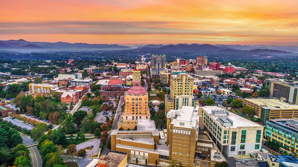 Gorgeous picture of downtown Asheville with sun setting over the blue ridge mountains of western North Carolina in the background.